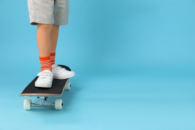 Photo of Little boy with skateboard on light blue background, closeup. Space for text