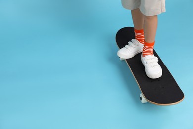 Little boy with skateboard on light blue background, closeup. Space for text