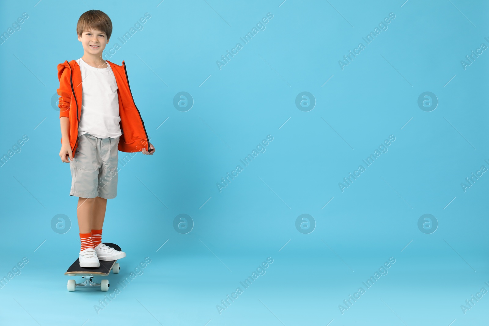 Photo of Little boy with skateboard on light blue background, space for text