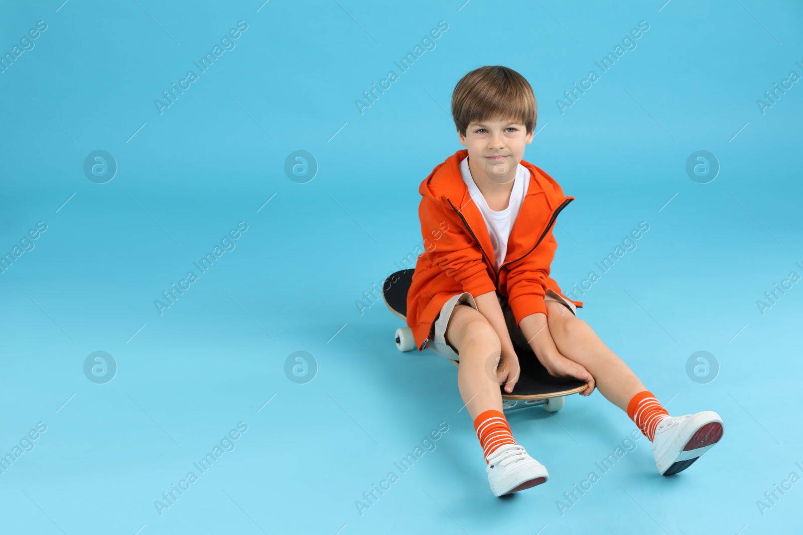 Photo of Little boy with skateboard on light blue background, space for text