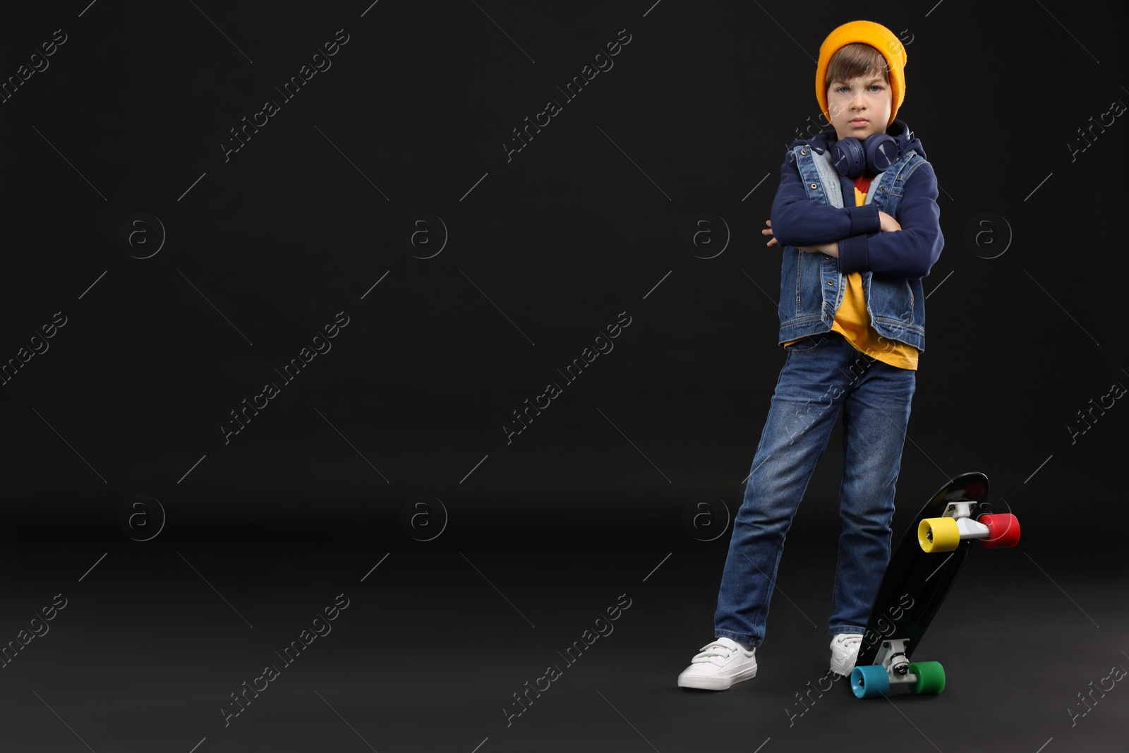 Photo of Little boy with skateboard on black background, space for text