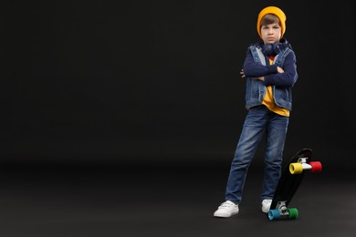 Little boy with skateboard on black background, space for text