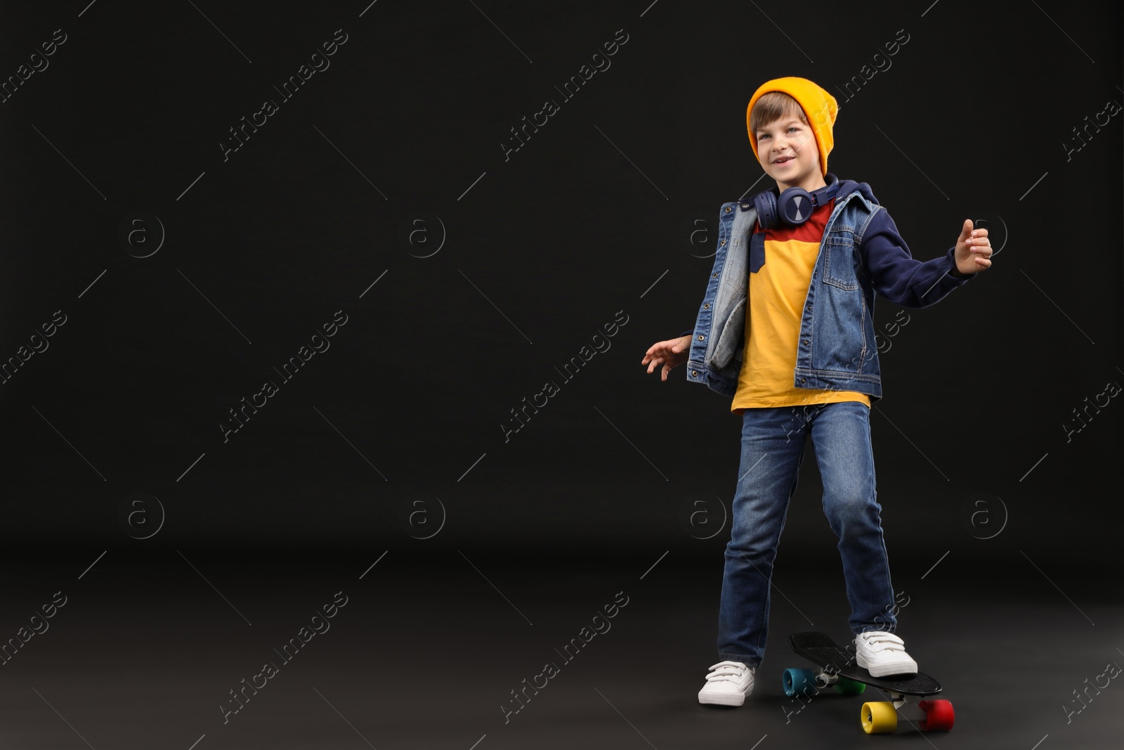 Photo of Little boy with skateboard on black background, space for text