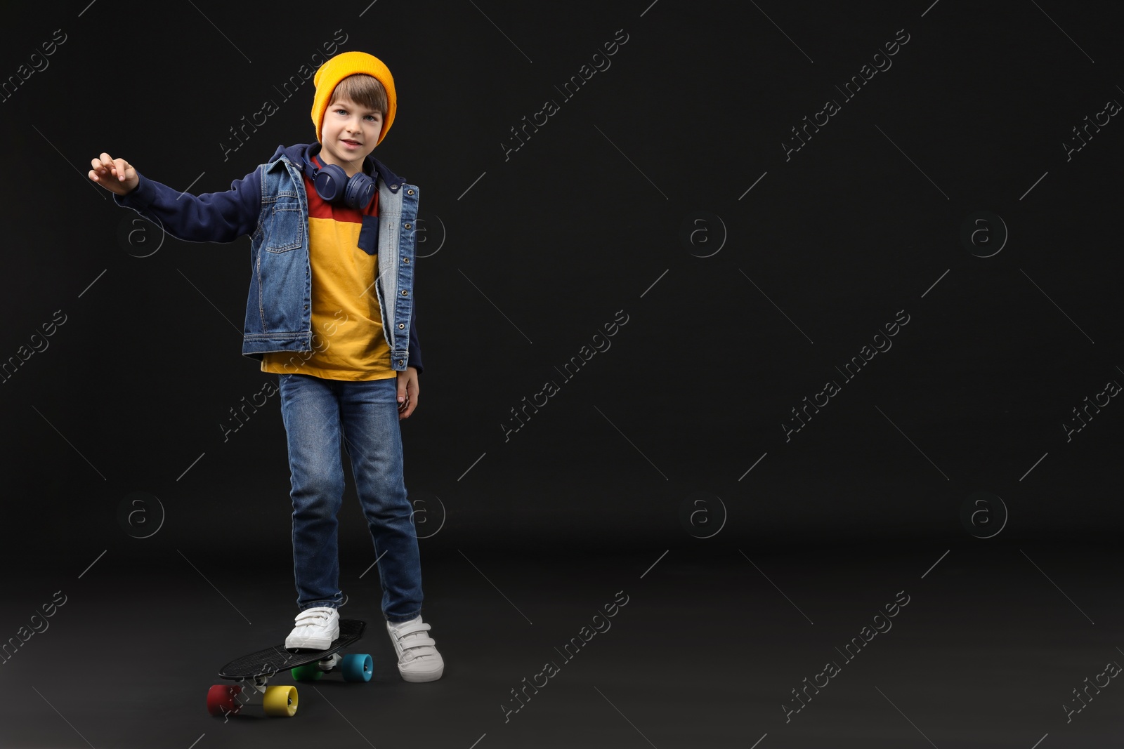 Photo of Little boy with skateboard on black background, space for text