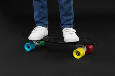 Photo of Little boy with skateboard on black background, closeup