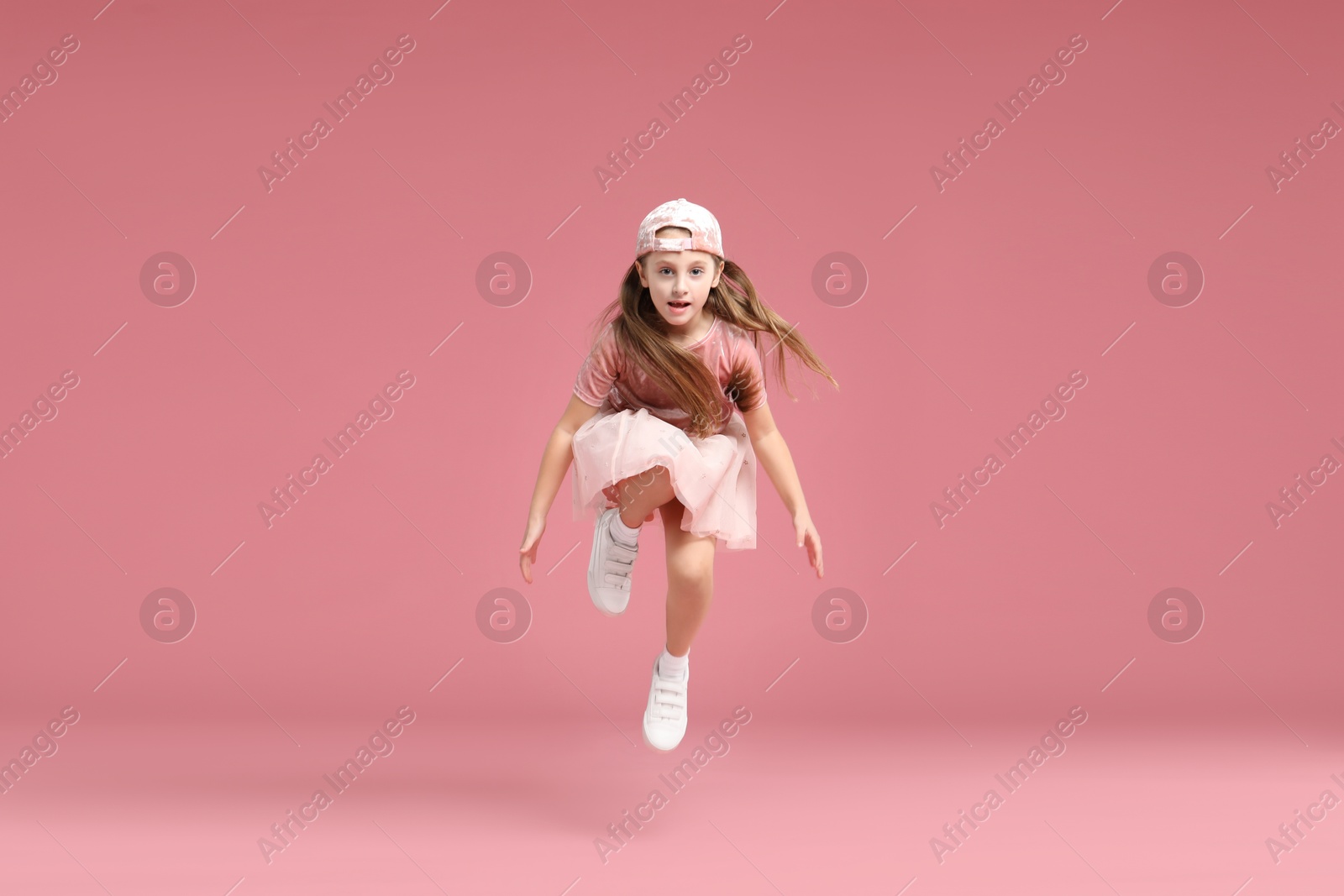 Photo of Cute little girl jumping on pink background