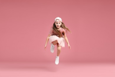 Photo of Cute little girl jumping on pink background