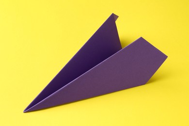 Photo of One handmade purple paper plane on yellow background, closeup