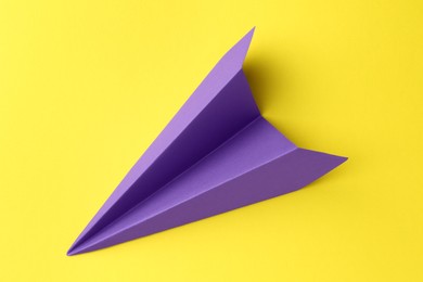 Photo of One handmade purple paper plane on yellow background, top view