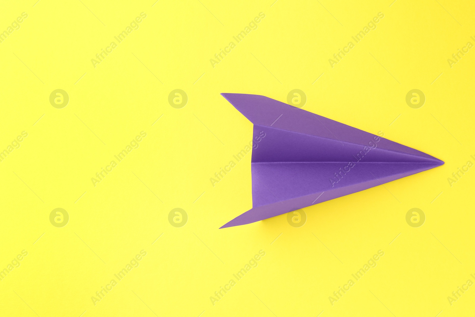 Photo of One handmade purple paper plane on yellow background, top view. Space for text