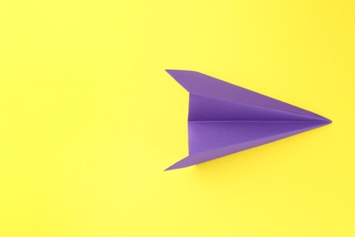 Photo of One handmade purple paper plane on yellow background, top view. Space for text