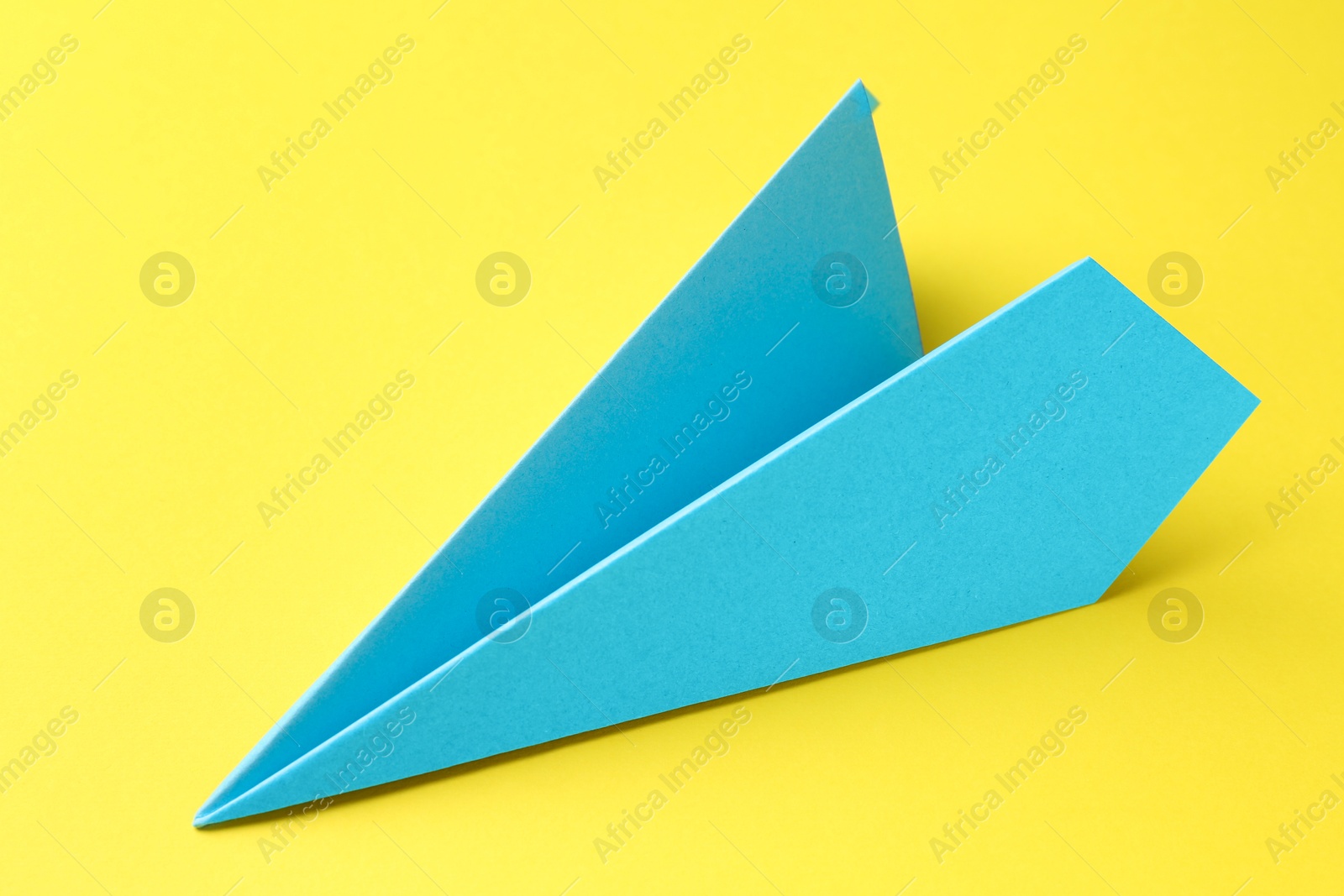 Photo of One handmade light blue paper plane on yellow background