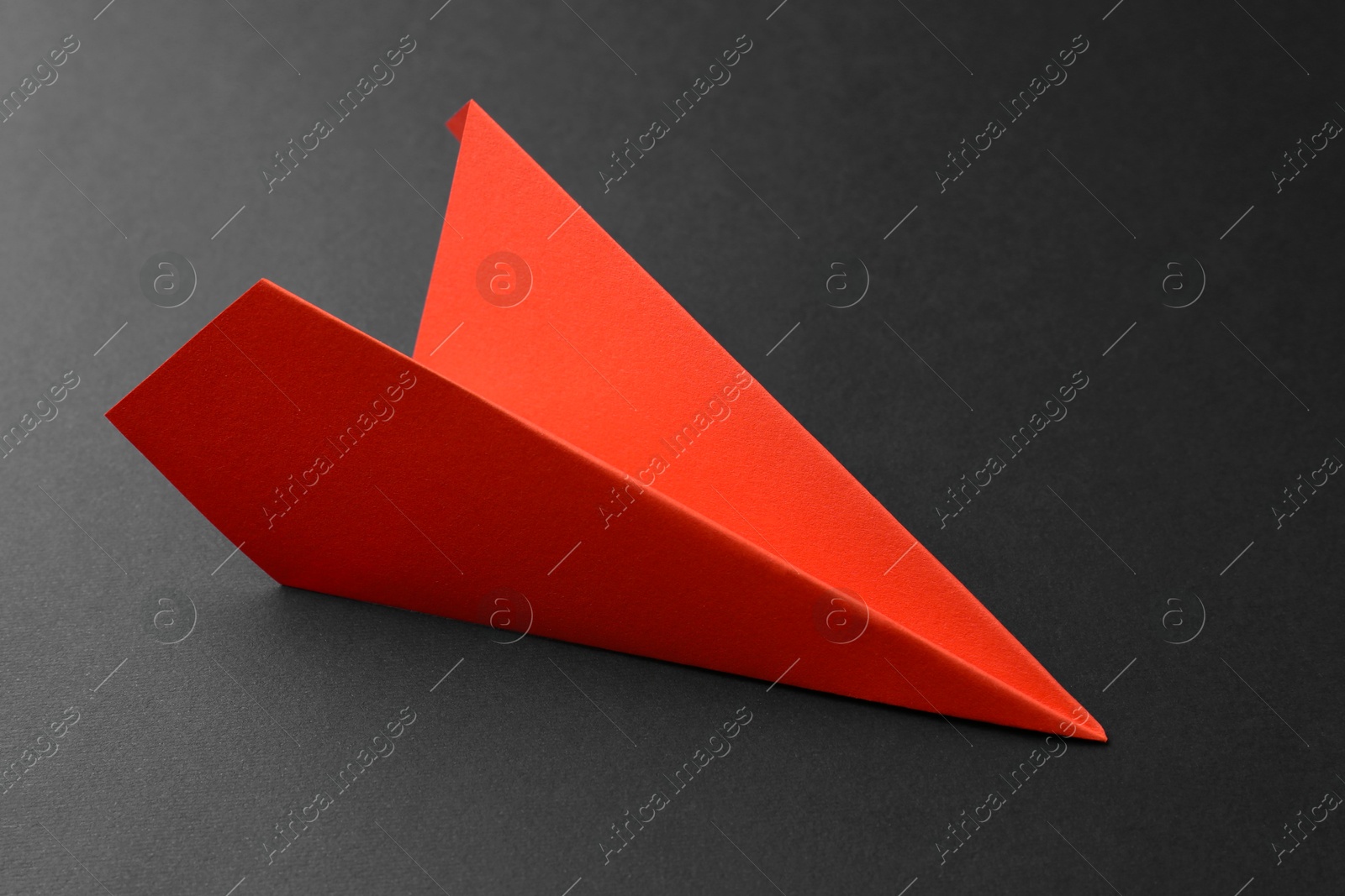 Photo of One handmade orange paper plane on grey background, closeup