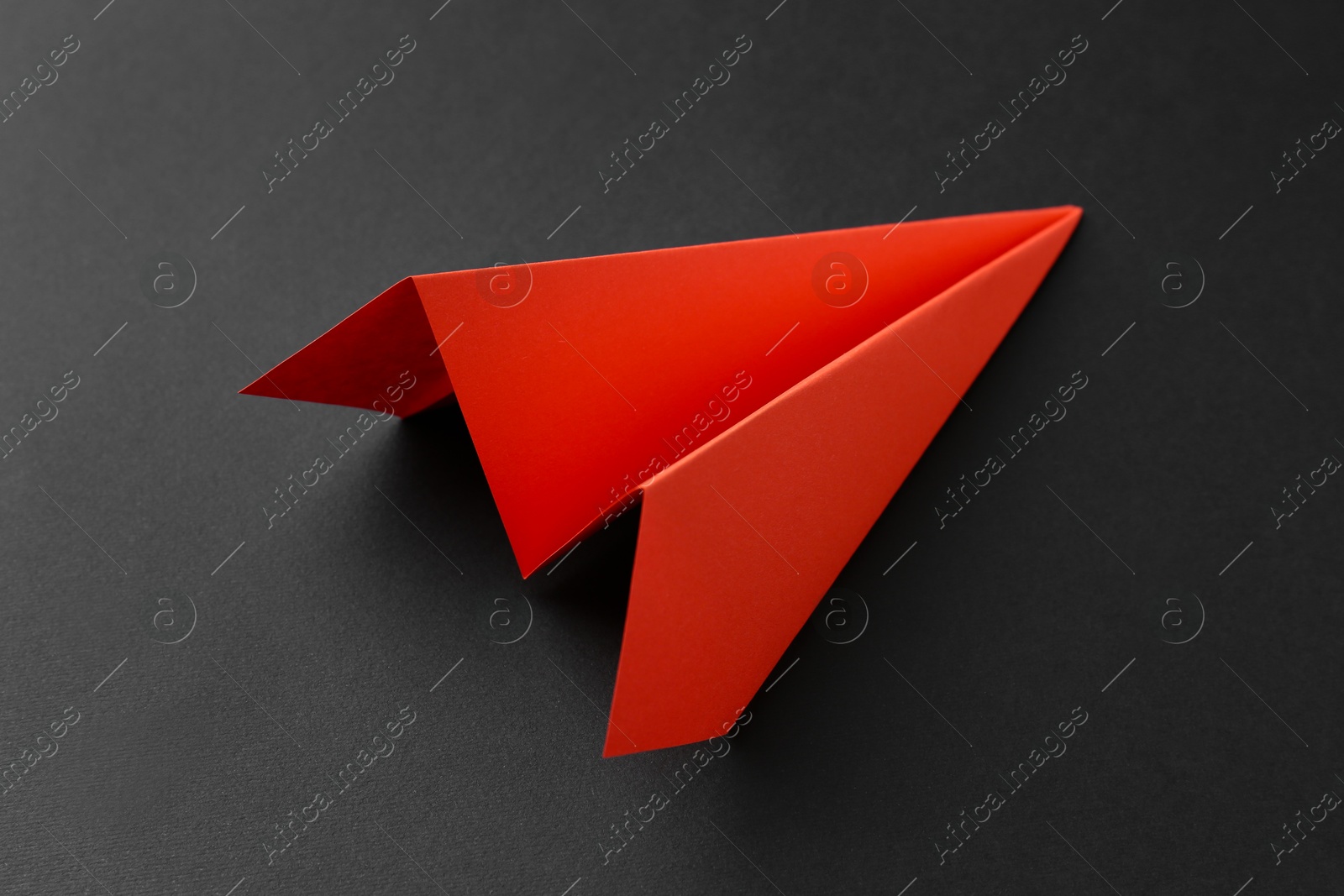 Photo of One handmade orange paper plane on grey background, closeup