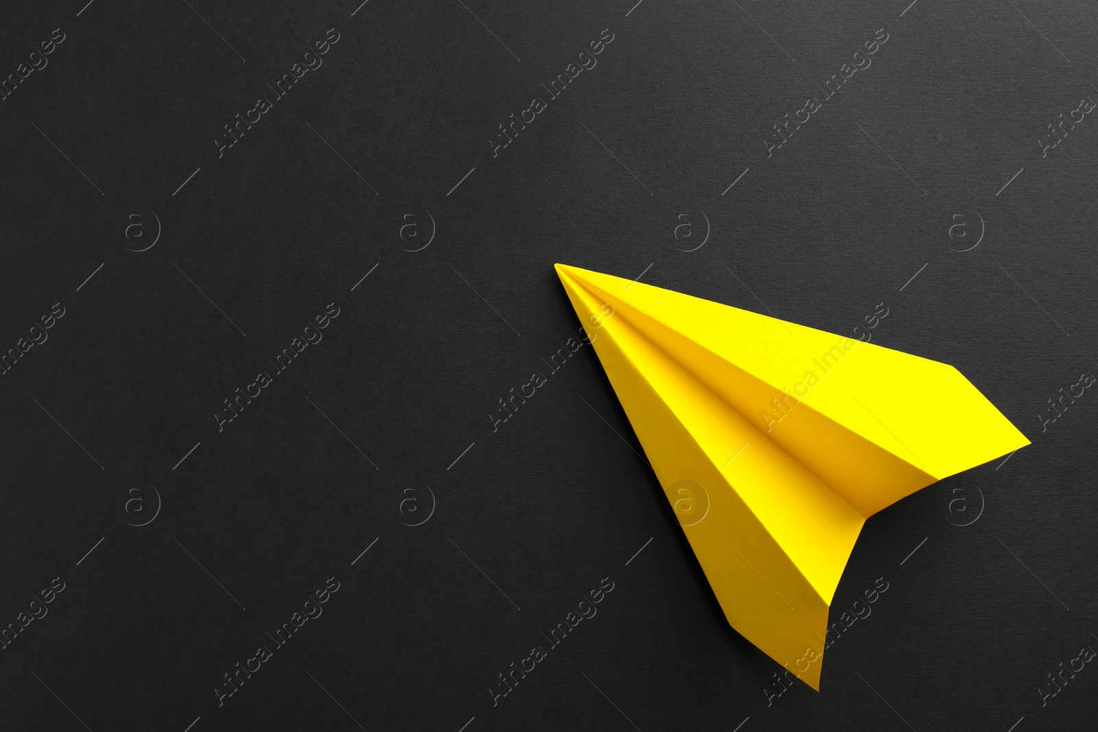 Photo of One handmade yellow paper plane on black background, top view. Space for text