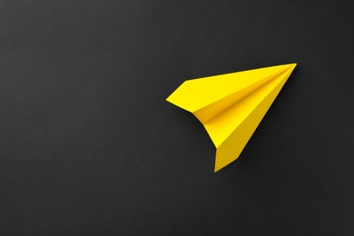 Photo of One handmade yellow paper plane on black background, top view. Space for text