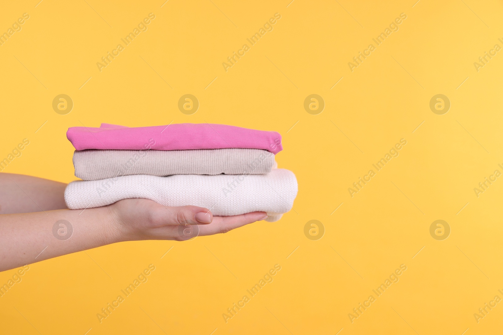 Photo of Woman holding stacked clothes on yellow background, closeup. Space for text