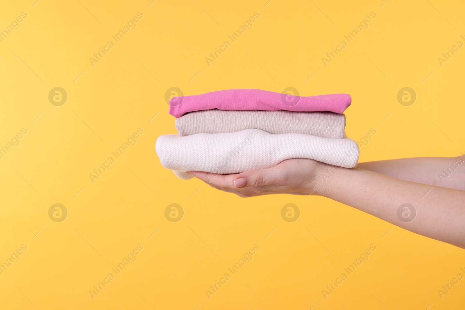 Photo of Woman holding stacked clothes on yellow background, closeup. Space for text