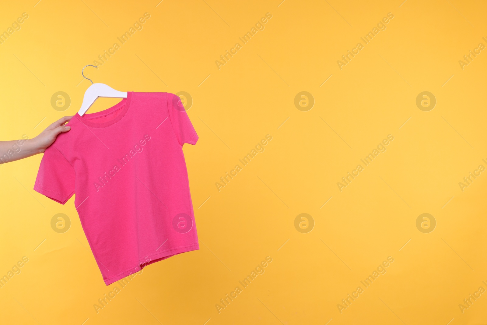 Photo of Woman holding hanger with pink t-shirt on yellow background, closeup. Space for text