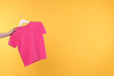 Photo of Woman holding hanger with pink t-shirt on yellow background, closeup. Space for text