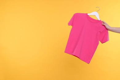 Photo of Woman holding hanger with pink t-shirt on yellow background, closeup. Space for text