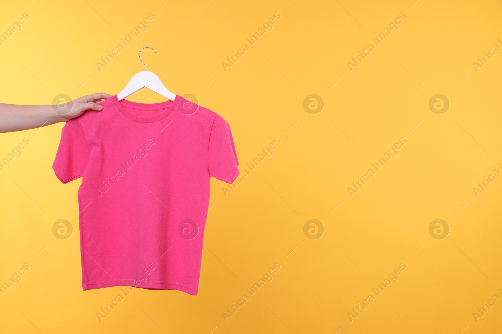 Photo of Woman holding hanger with pink t-shirt on yellow background, closeup. Space for text