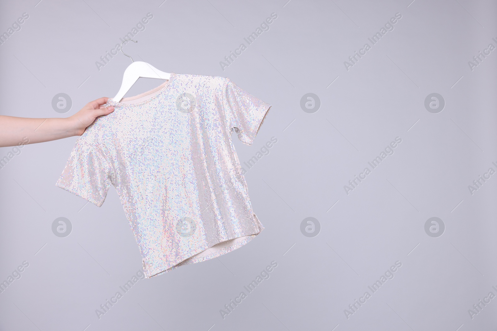 Photo of Woman holding hanger with stylish t-shirt on light grey background, closeup. Space for text