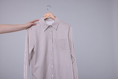 Photo of Woman holding hanger with stylish shirt on light grey background, closeup. Space for text