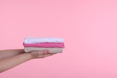 Photo of Woman holding stacked clothes on pink background, closeup. Space for text