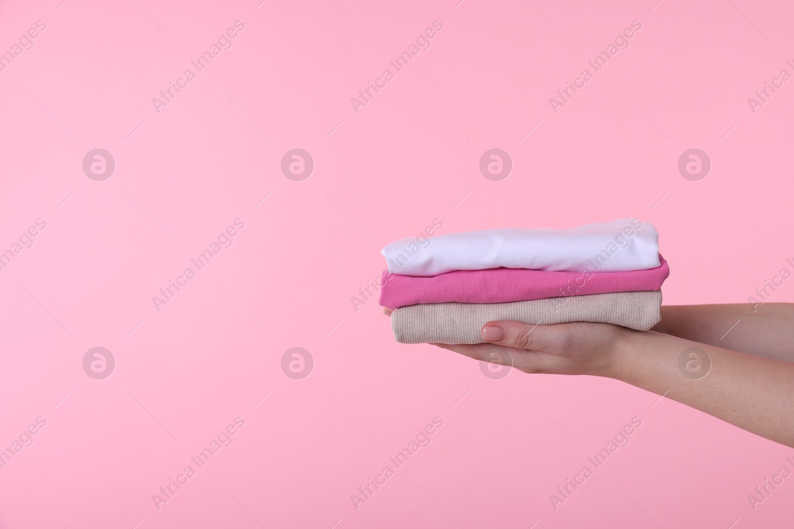 Photo of Woman holding stacked clothes on pink background, closeup. Space for text