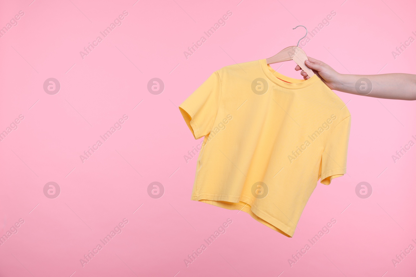 Photo of Woman holding hanger with yellow t-shirt on pink background, closeup. Space for text