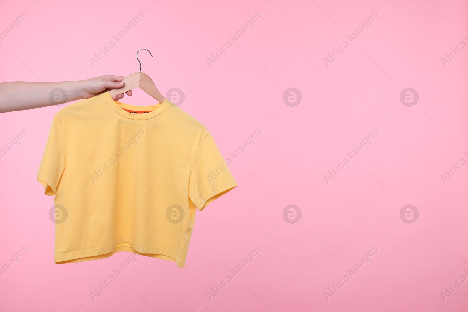 Photo of Woman holding hanger with yellow t-shirt on pink background, closeup. Space for text