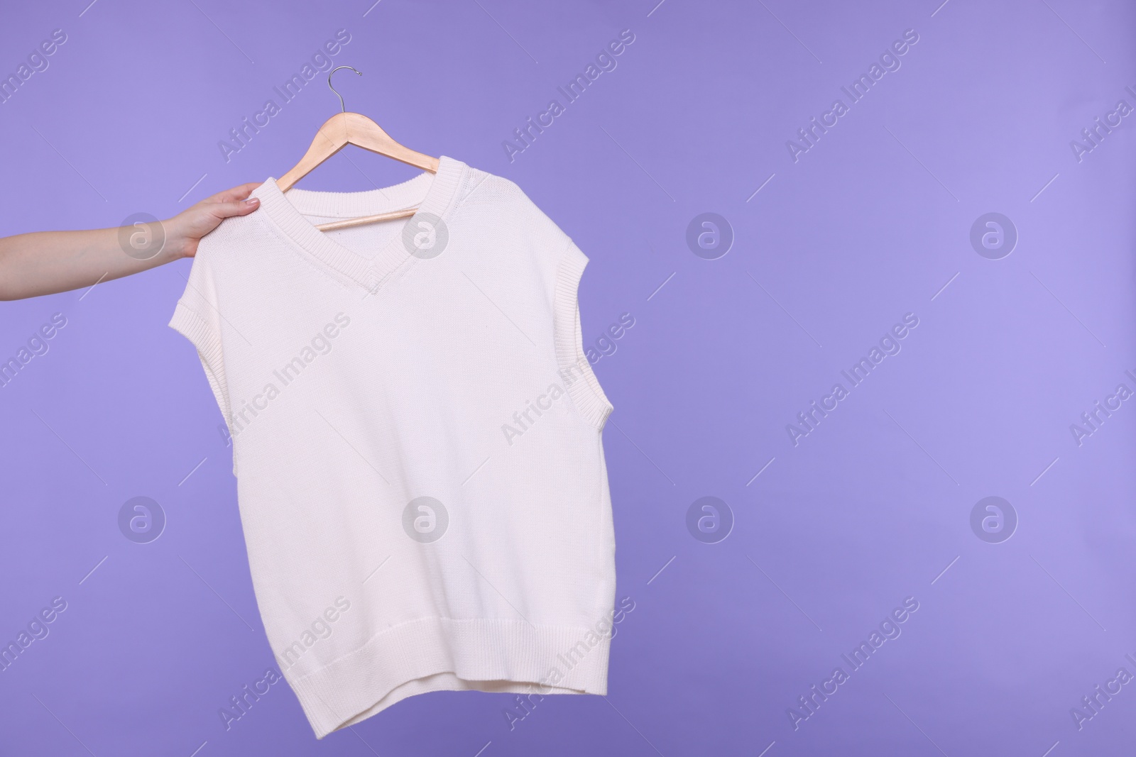 Photo of Woman holding hanger with sweater vest on light purple background, closeup. Space for text