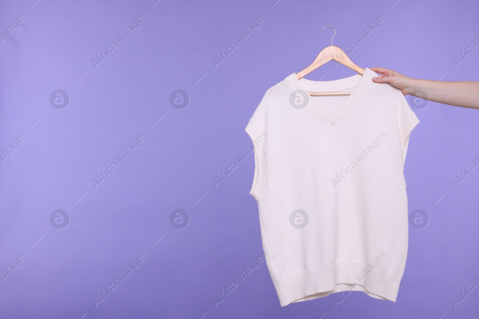 Photo of Woman holding hanger with sweater vest on light purple background, closeup. Space for text