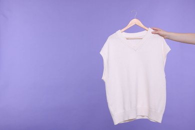 Photo of Woman holding hanger with sweater vest on light purple background, closeup. Space for text