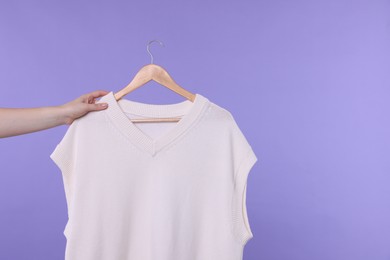 Photo of Woman holding hanger with sweater vest on light purple background, closeup. Space for text