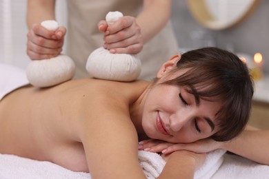 Photo of Young woman receiving massage with herbal bags in spa salon