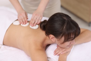 Photo of Young woman receiving hot stone massage in spa salon