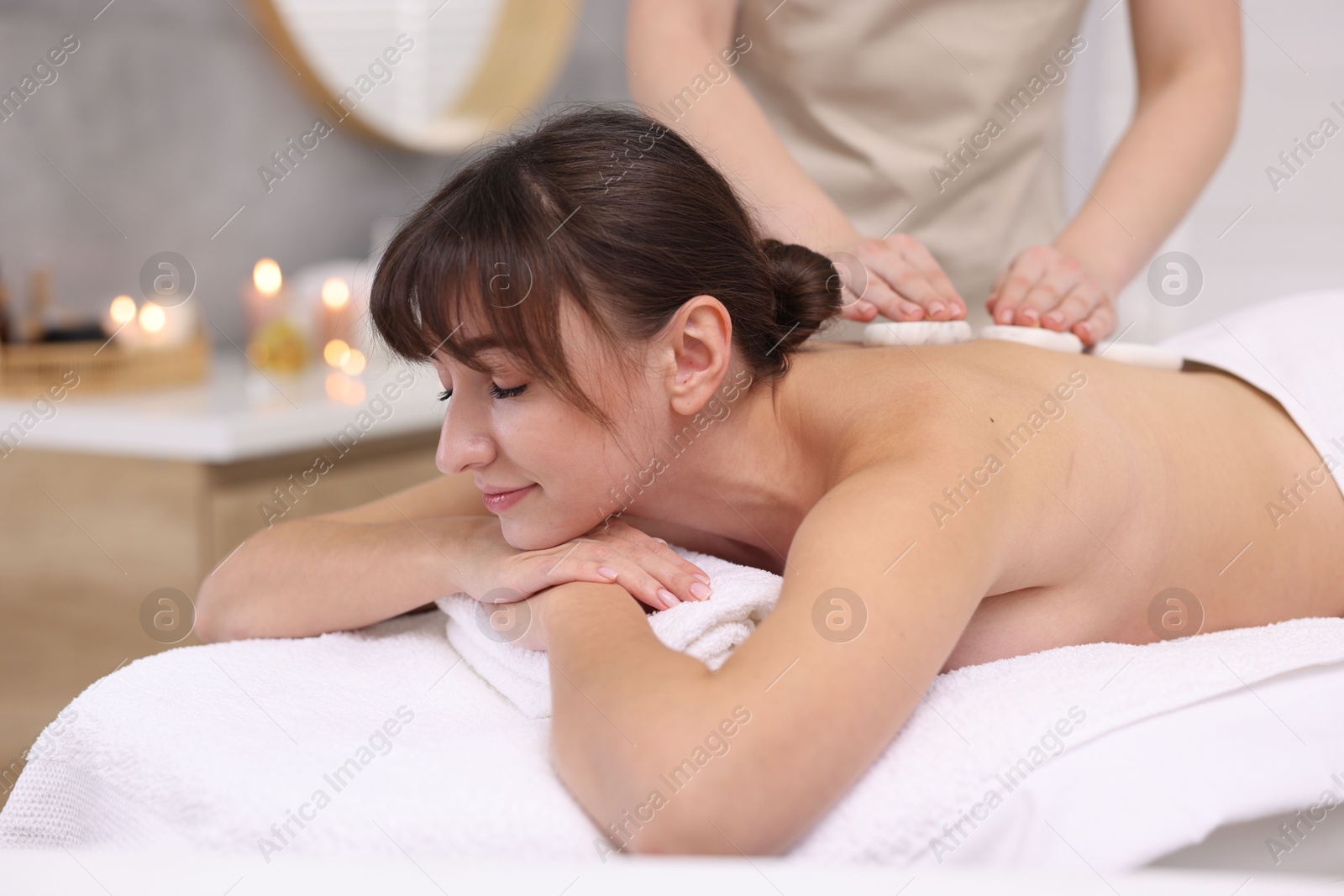 Photo of Young woman receiving hot stone massage in spa salon