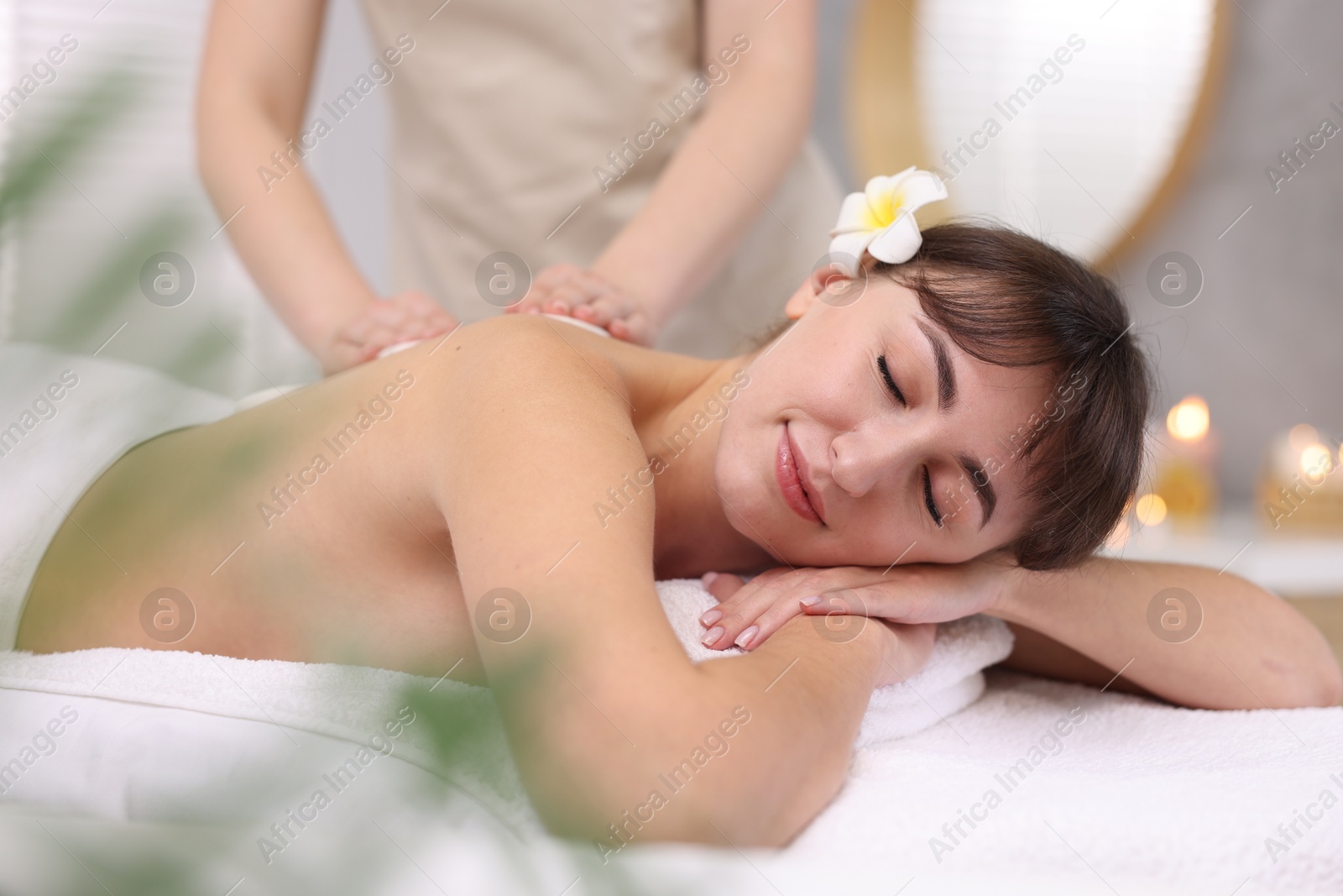 Photo of Young woman receiving hot stone massage in spa salon