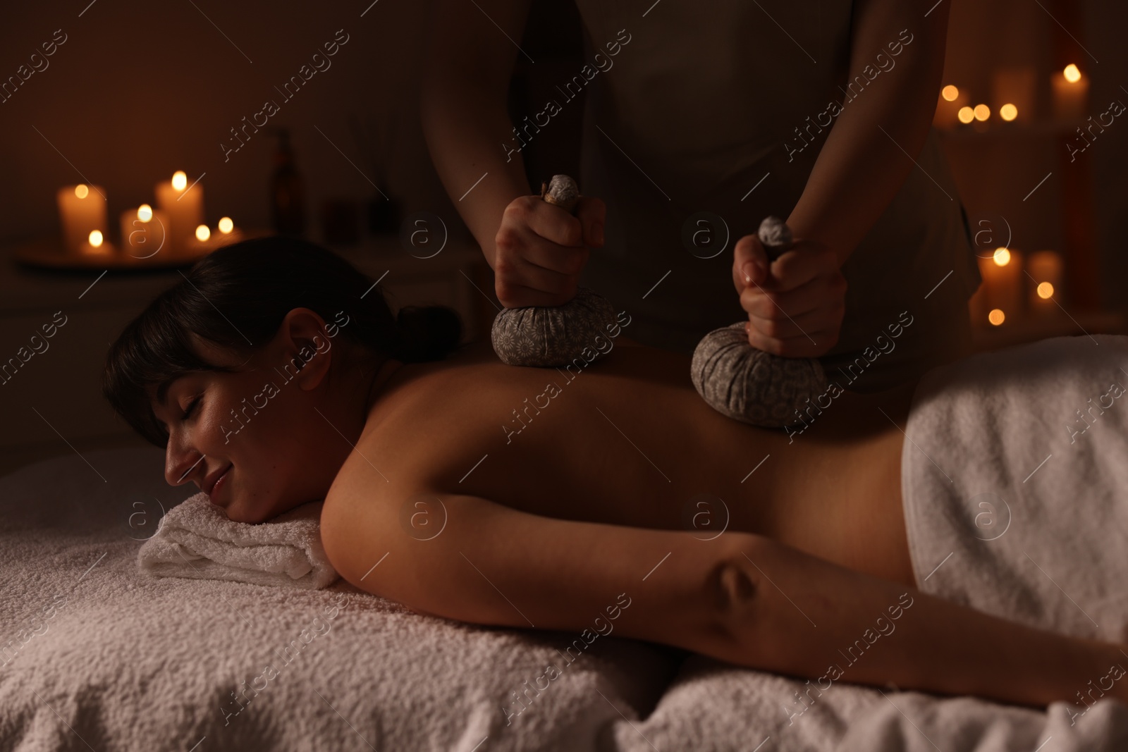 Photo of Young woman receiving back massage with herbal bags in spa salon