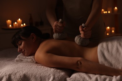 Photo of Young woman receiving back massage with herbal bags in spa salon