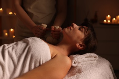 Photo of Young woman receiving massage with herbal bags in spa salon