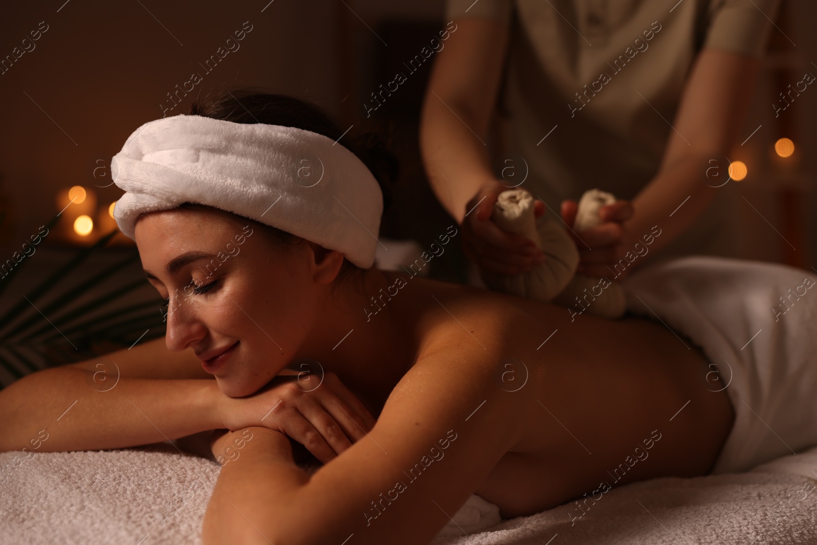 Photo of Young woman receiving back massage with herbal bags in spa salon