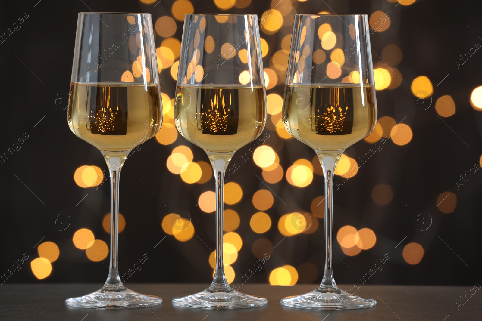 Photo of Glasses of luxury white wine on wooden table against dark background with blurred lights. Bokeh effect