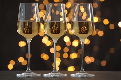 Photo of Glasses of luxury white wine on wooden table against dark background with blurred lights. Bokeh effect