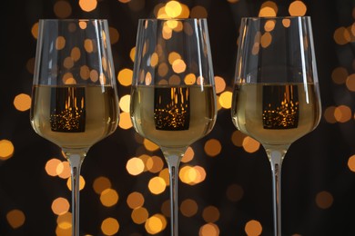 Photo of Glasses of luxury white wine against dark background with blurred lights, closeup. Bokeh effect