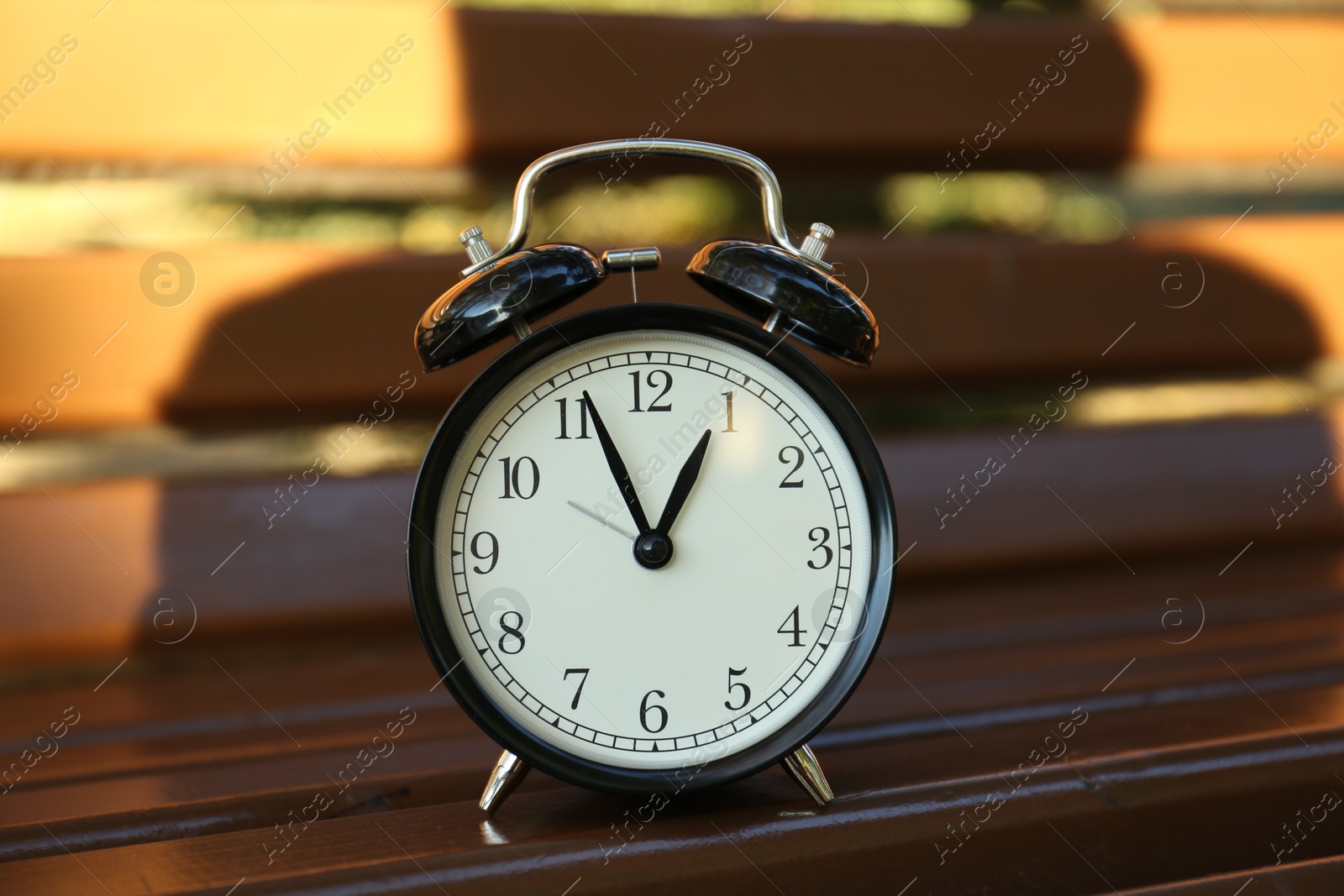 Photo of One alarm clock on wooden bench outdoors