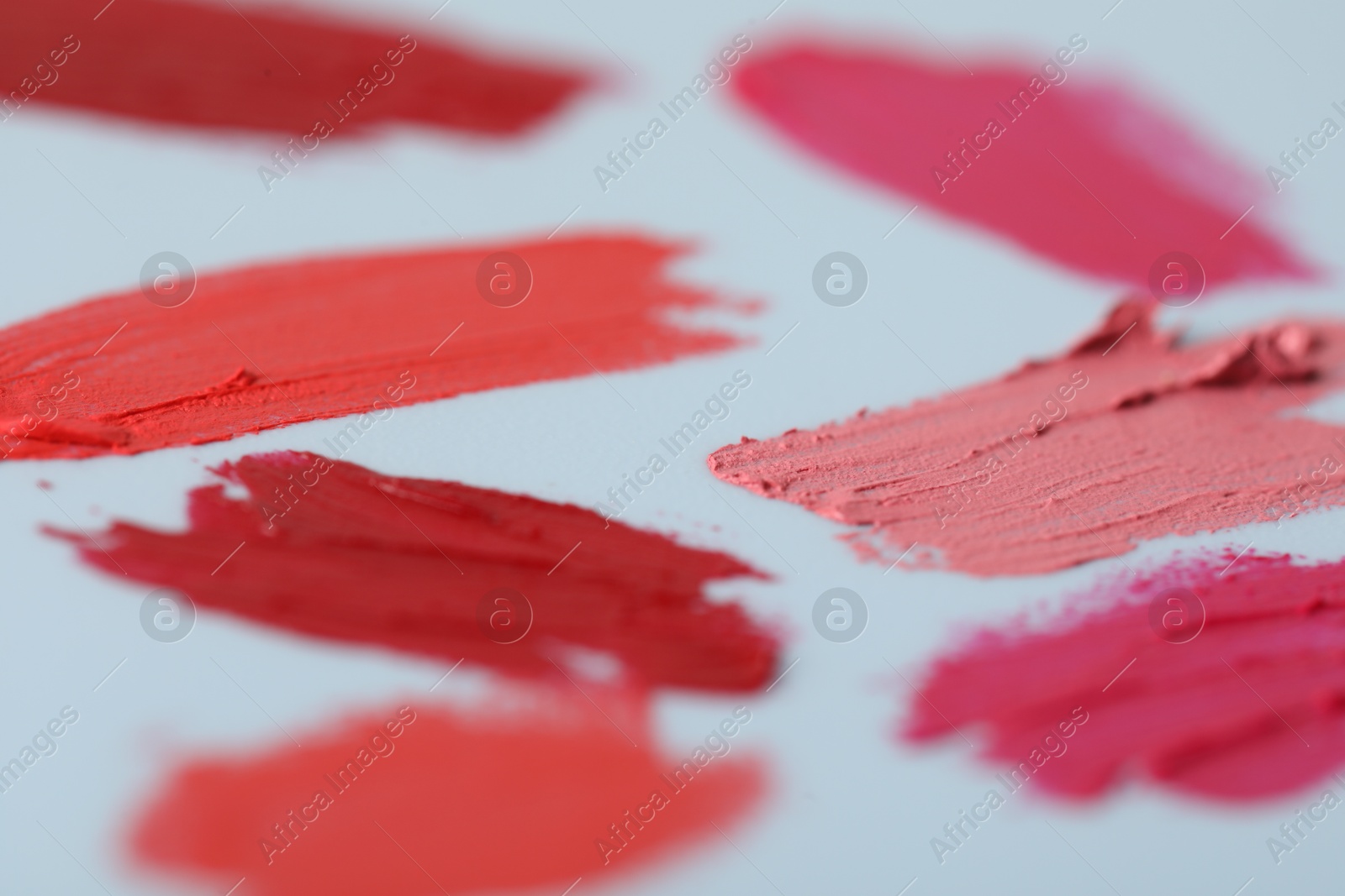 Photo of Samples of bright lipsticks on light blue background, closeup