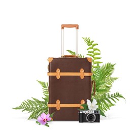 Brown travel suitcase, camera, tropical leaves and flowers on white background